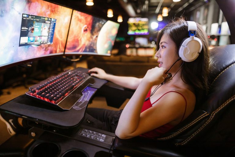 Young woman in red top gaming on dual monitors with white headphones in a modern setup. — Casino Games Offering Flexible Wage