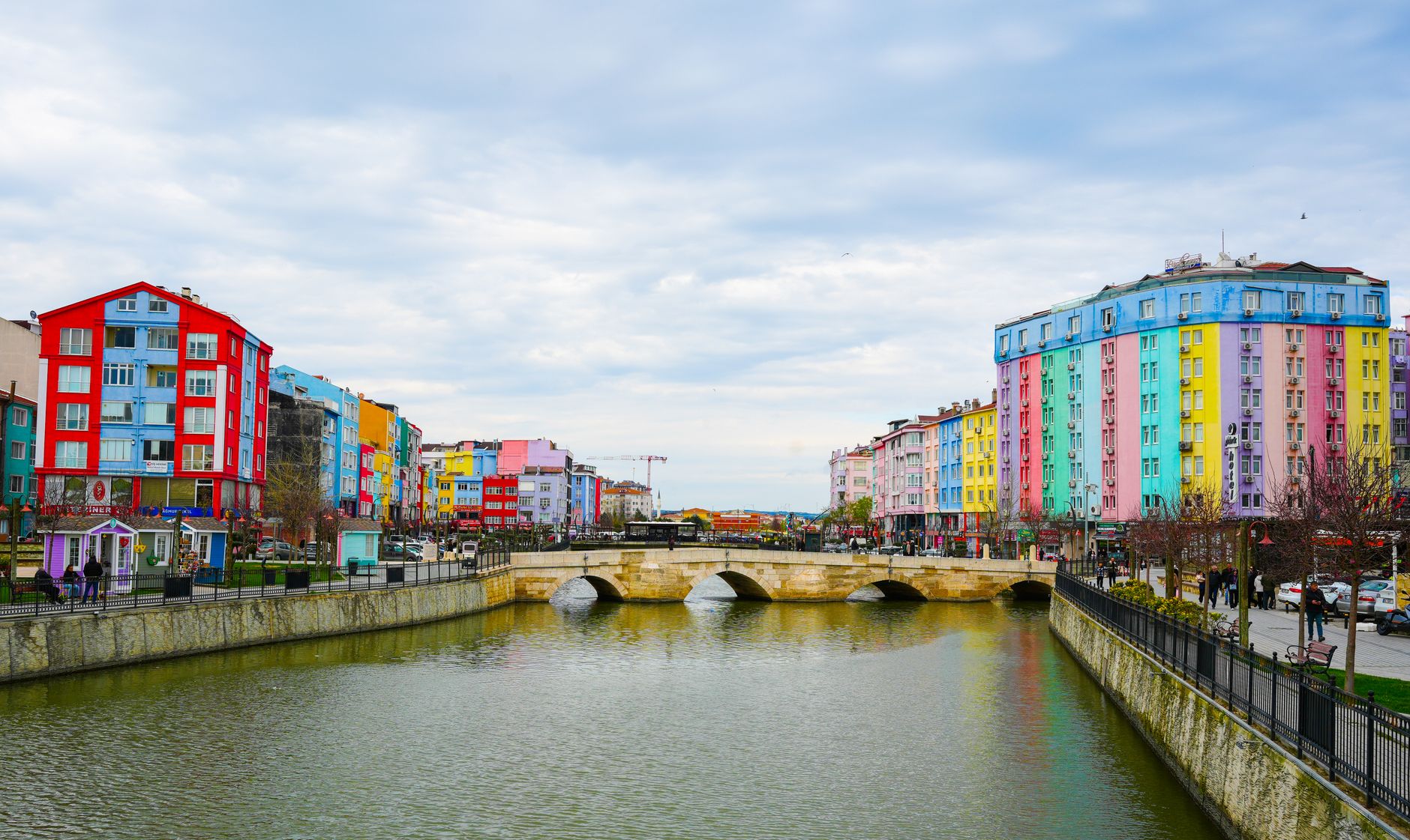 Vibrant cityscape with colorful buildings along a river and stone bridge under a cloudy sky. — Die Atmosphäre des Jokery Casi