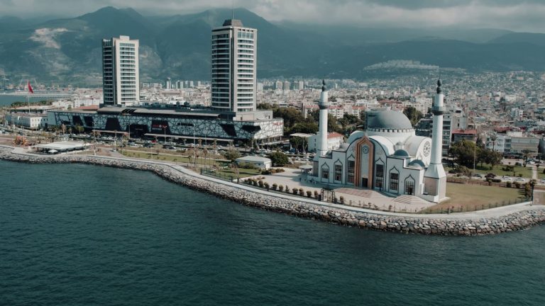 Aerial photograph showcasing İskenderun's mosque and cityscape against the mountainous backdrop on a sunny day. — Die aufrege