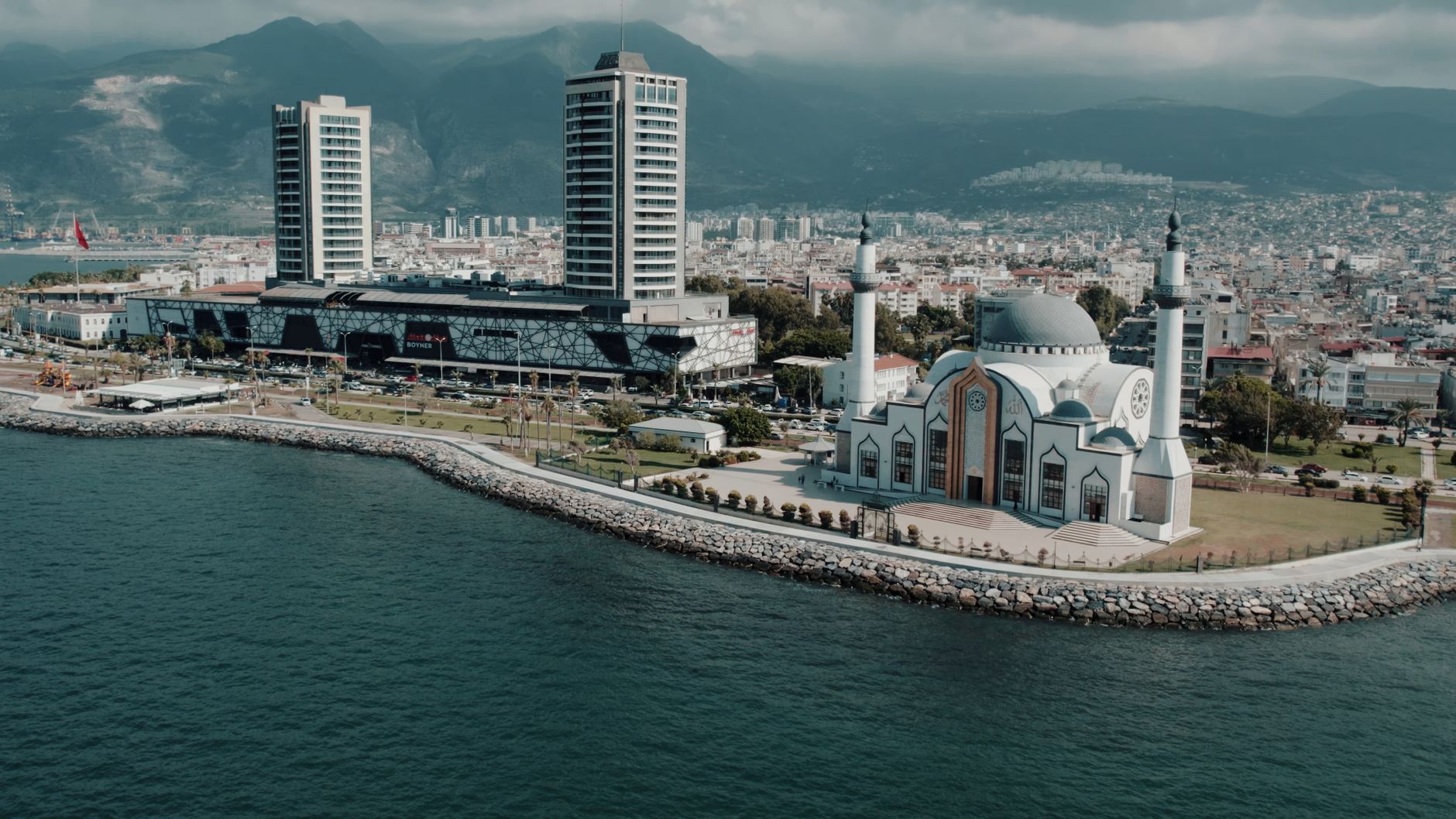 Aerial photograph showcasing İskenderun's mosque and cityscape against the mountainous backdrop on a sunny day. — Die aufrege