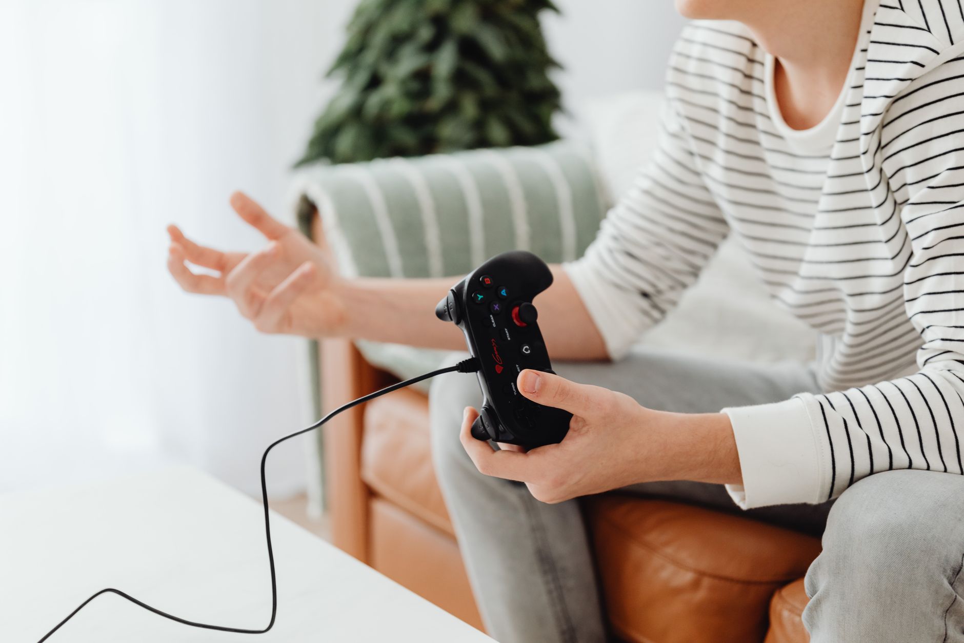Close-up of a person playing video games at home with a wired controller on a couch. — Different Ways to Play Online Baccarat