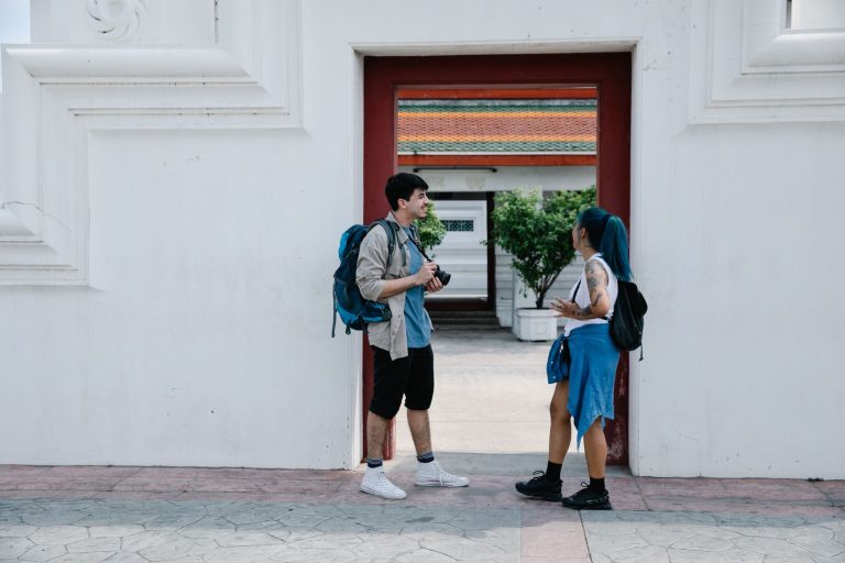 Two young travelers with backpacks share a moment at a cultural landmark, blending contemporary style with tradition. — Explo