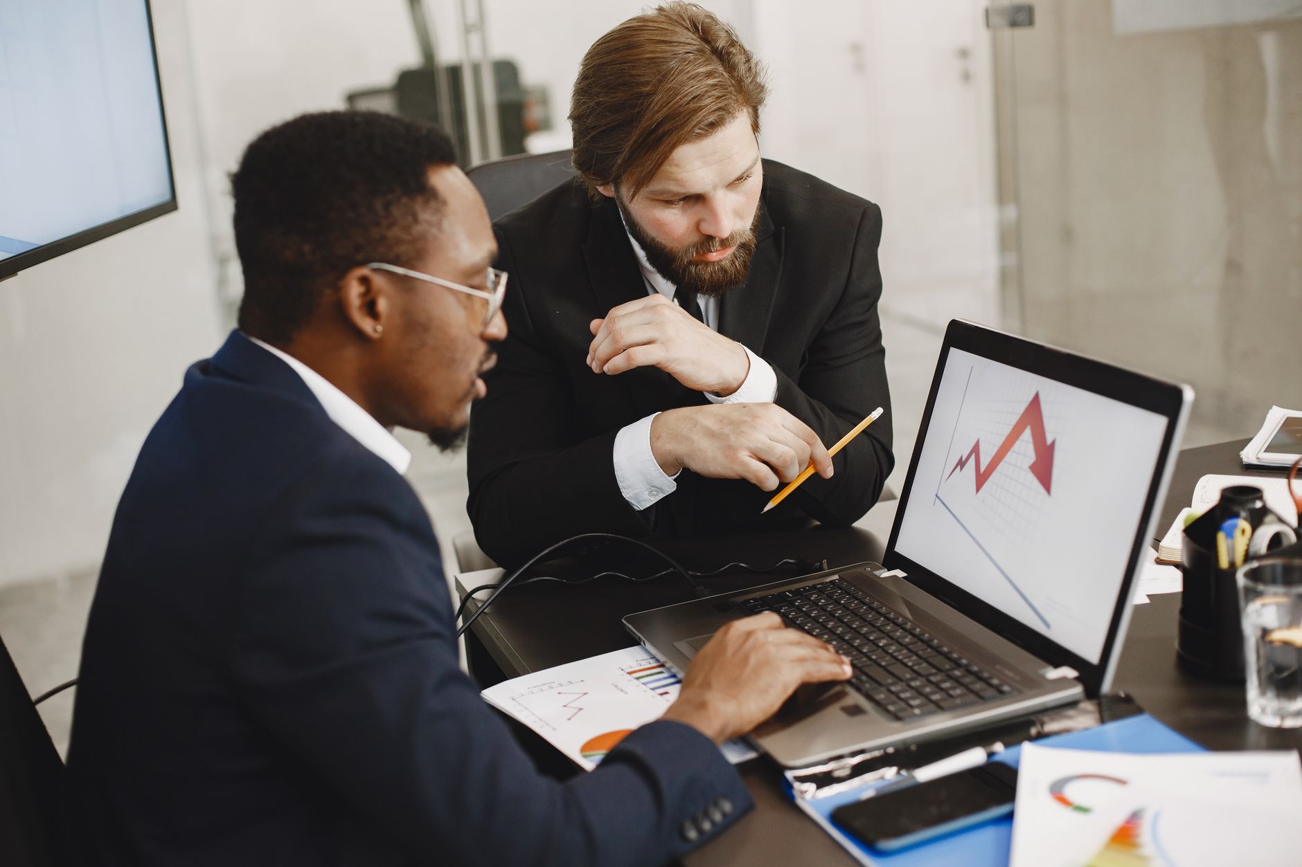 Two business professionals discuss marketing data on a laptop in a modern office. — Factors That Determines the Best Forex Br