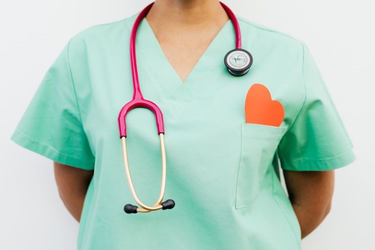 Close-up of a medical professional with a stethoscope and a paper heart cutout on a green uniform pocket. — From Passion to P