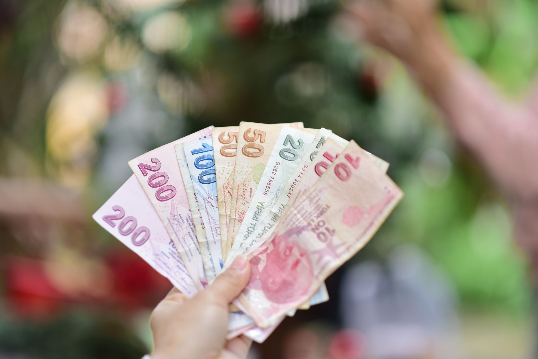 A hand holding multiple Turkish Lira banknotes in an outdoor setting, showcasing various denominations. — Fünf Aspekte, die C
