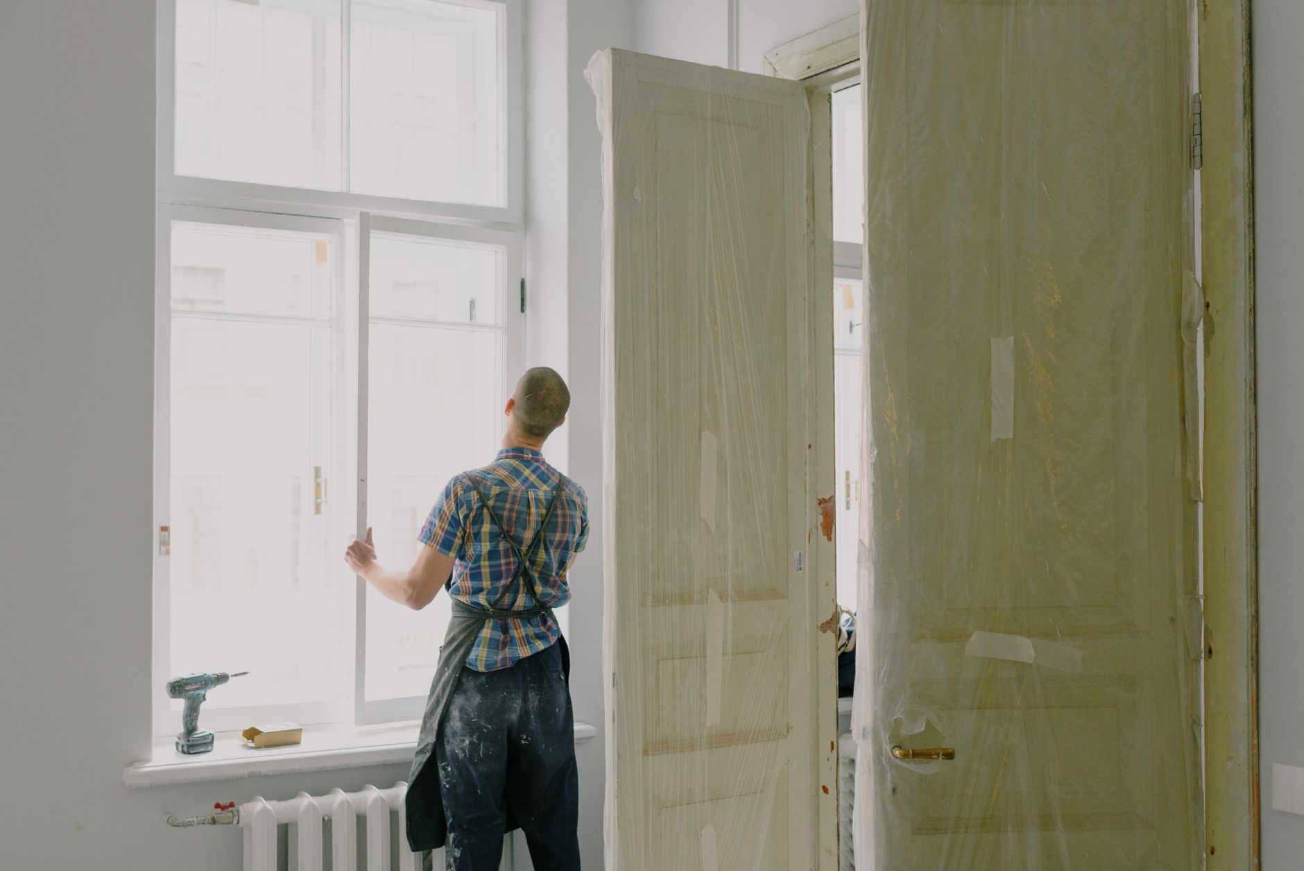 Back view of unrecognizable workman in apron mounting window near drilling machine and doors in flat — GARDEN BEAUTIFICATION: