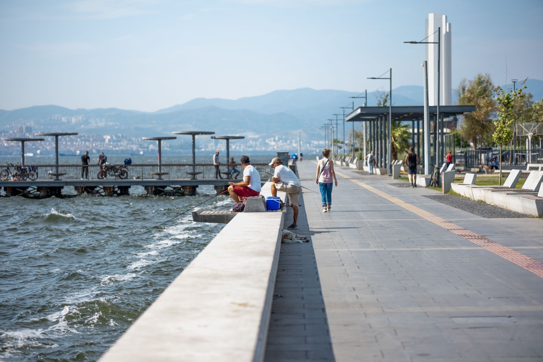 Serene seaside promenade with people fishing and strolling by the pier, set against coastal views. — Get the Best Aromatherap