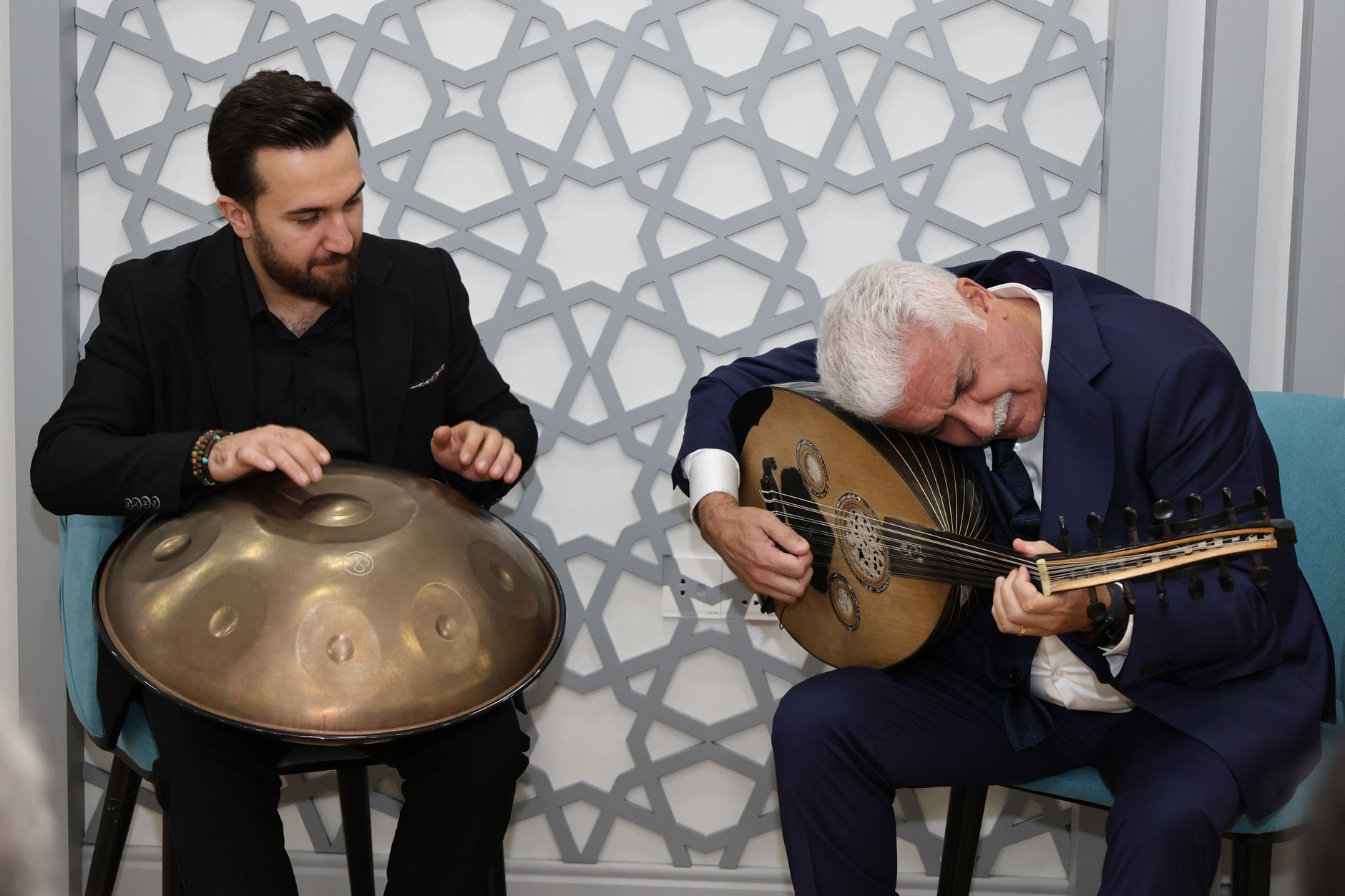 Two musicians playing oud and handpan in a cozy indoor setting, conveying cultural richness and musical harmony. — Go Beyond