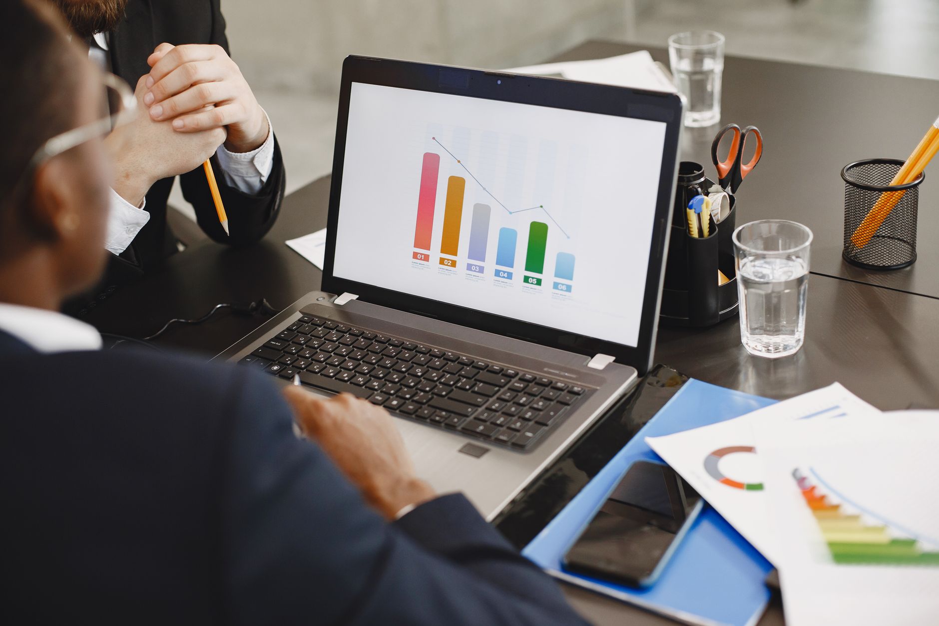 Two professionals analyzing a business graph on a laptop during a meeting. — H-1B Visa: A Great Guide American Employers and