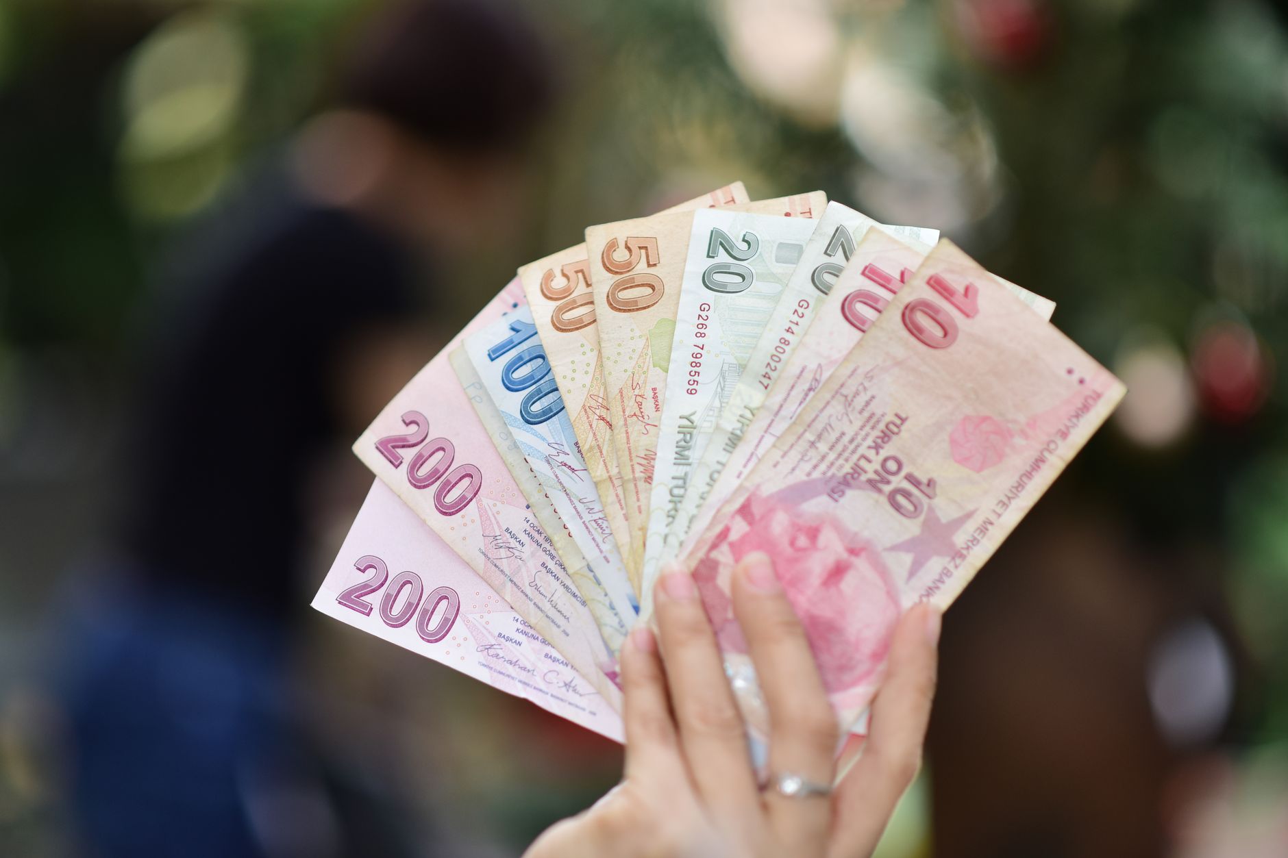 A hand holding various Turkish Lira banknotes with a blurred outdoor background. — Highest Rated Telugu movies in South India