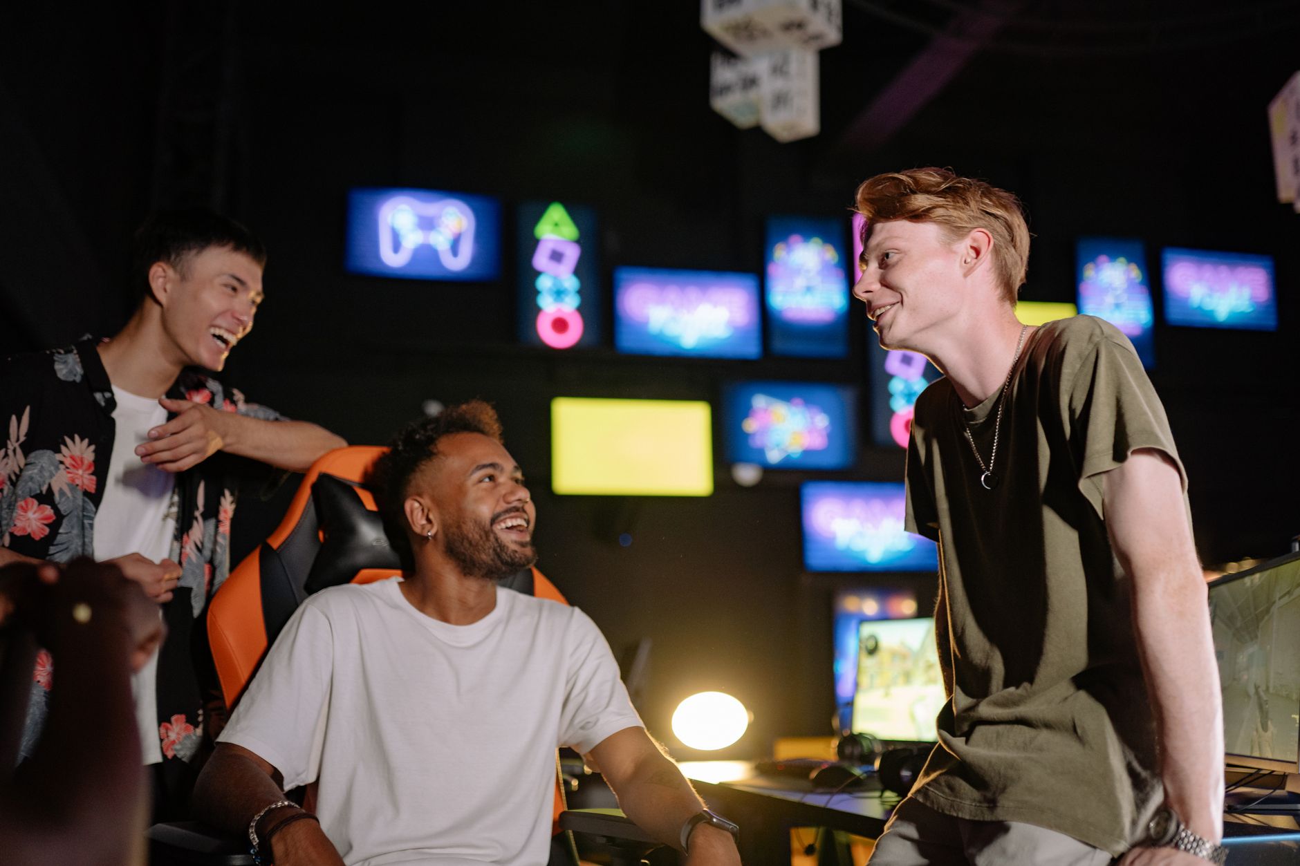 Three young men laughing and enjoying a gaming session in a vibrant room with multiple screens. — How can I make an accurate