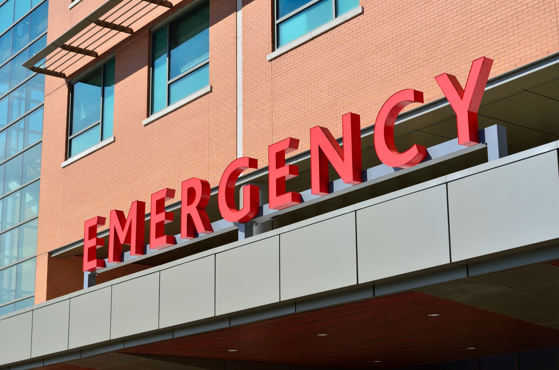 Close-up of a modern hospital emergency room entrance with prominent red letters. — How To Buy Weed In America - How To Decid