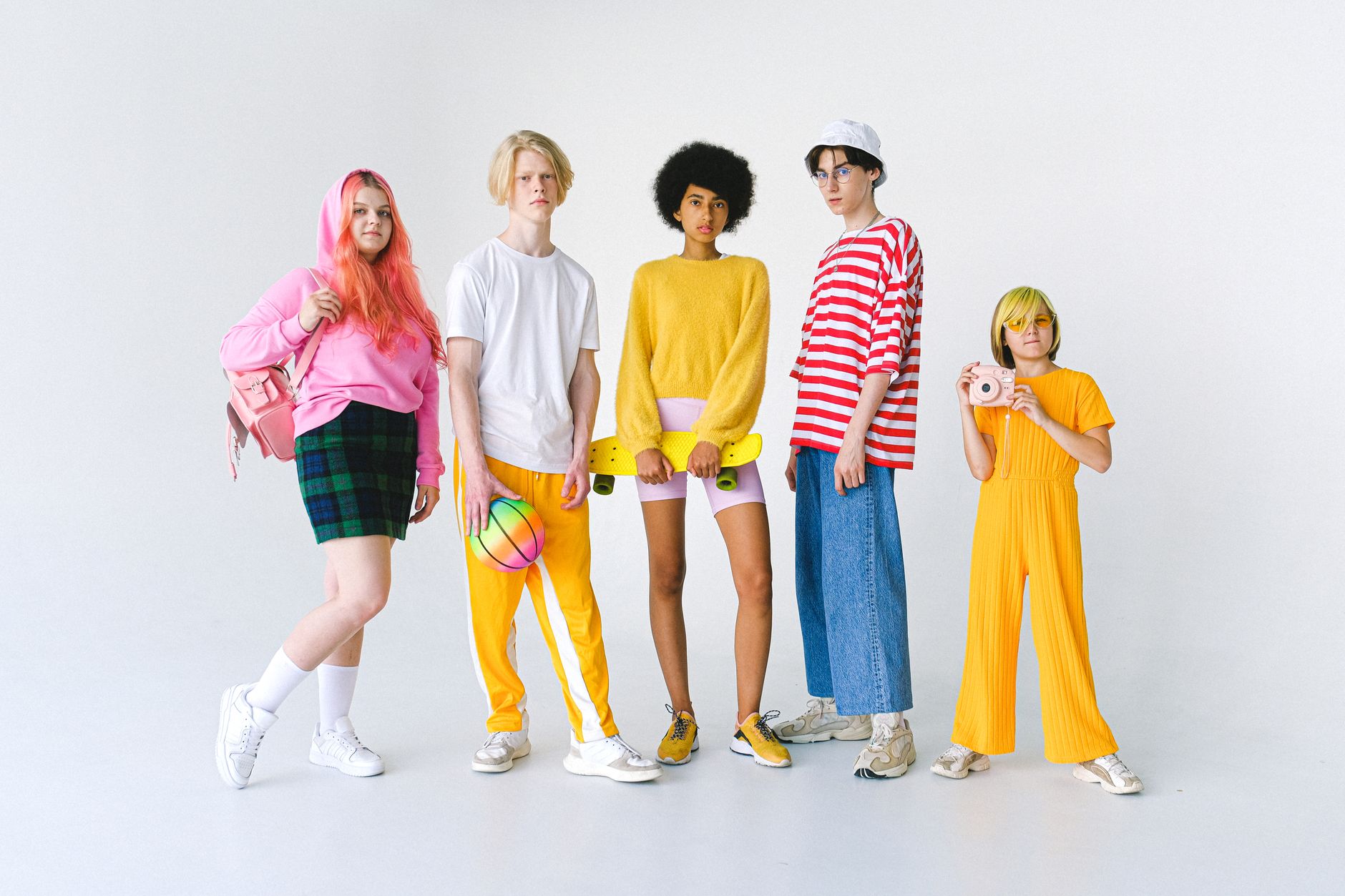 Full body group of informal teenager friends in colorful outfits standing against white background with ball and penny board
