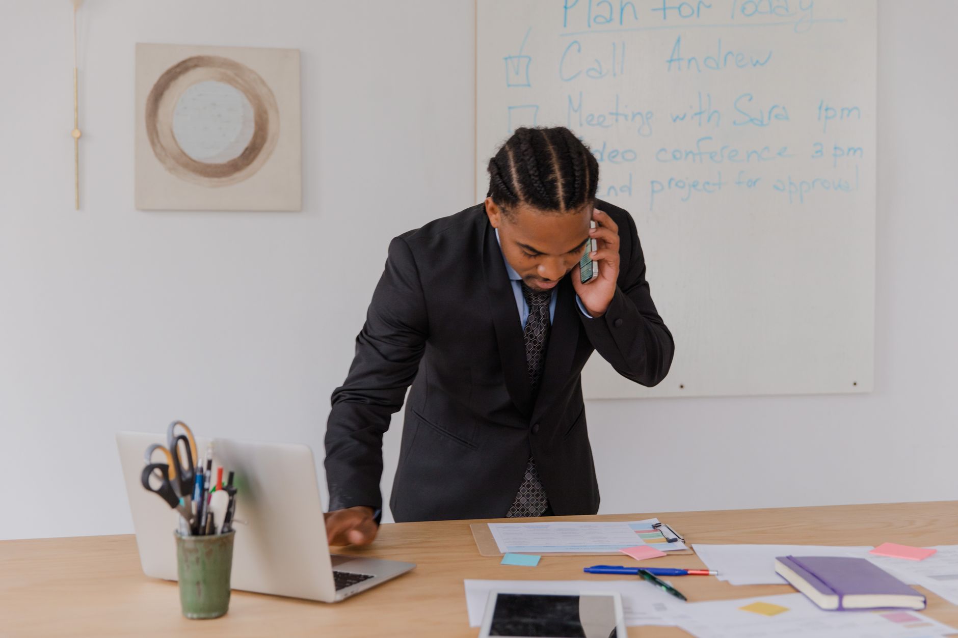 Professional businessman multitasking with phone and laptop at office desk, surrounded by documents. — Know about which is be