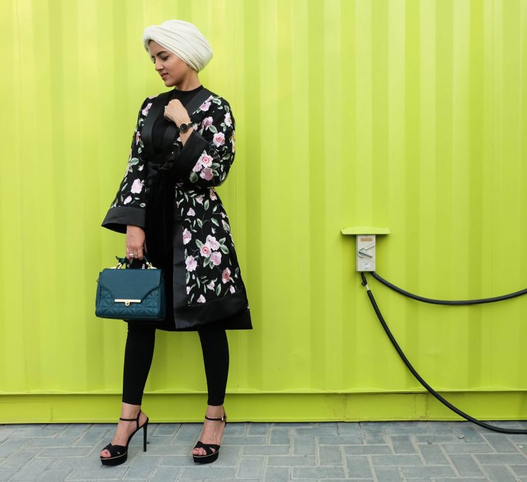 Fashionable woman in a floral coat and hijab standing with a green bag in Dubai. — Limites transactionnelles chez Locowin Cas