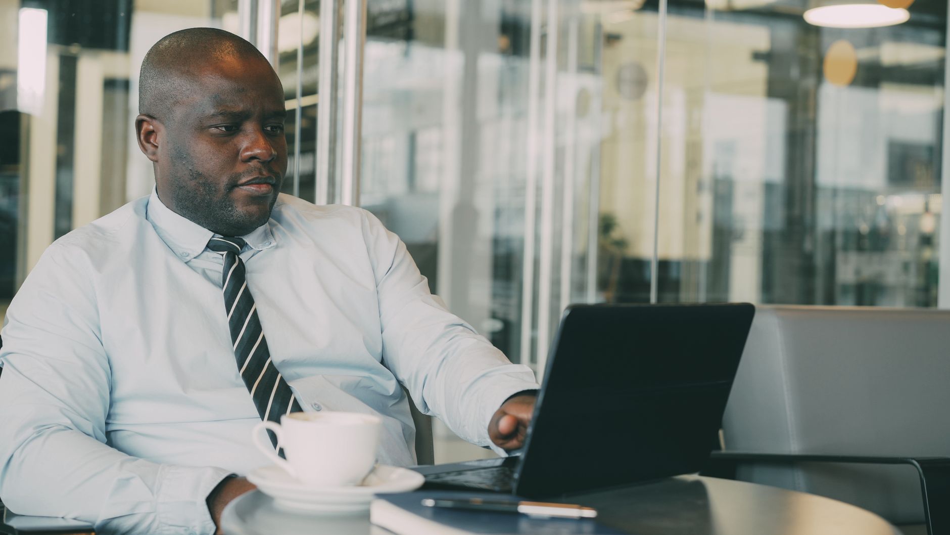 Focused businessman uses laptop in stylish cafe, sipping coffee. Perfect for business or lifestyle themes. — Lower Operating