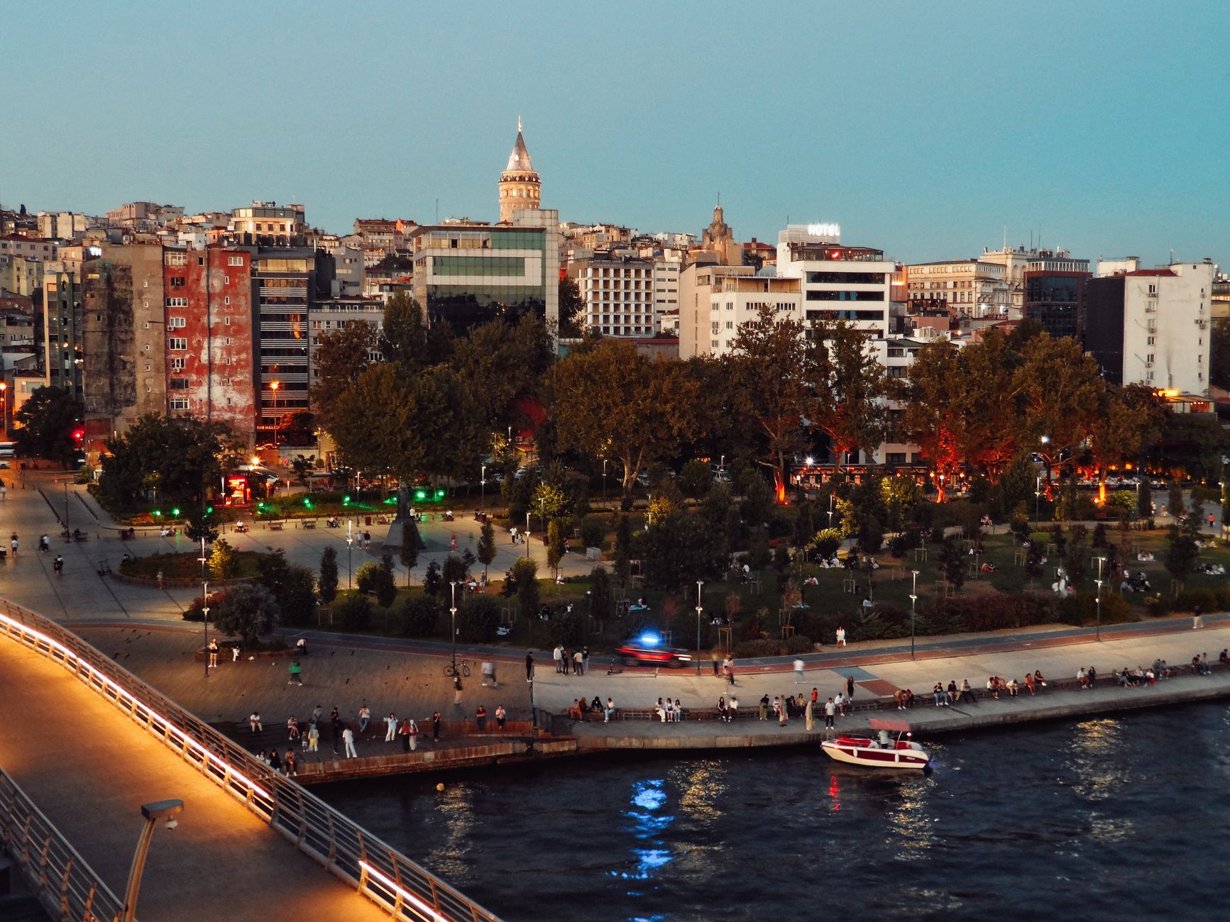 Scenic view of Istanbul's skyline featuring Galata Tower and bustling park at twilight along the waterfront. — Navigating the