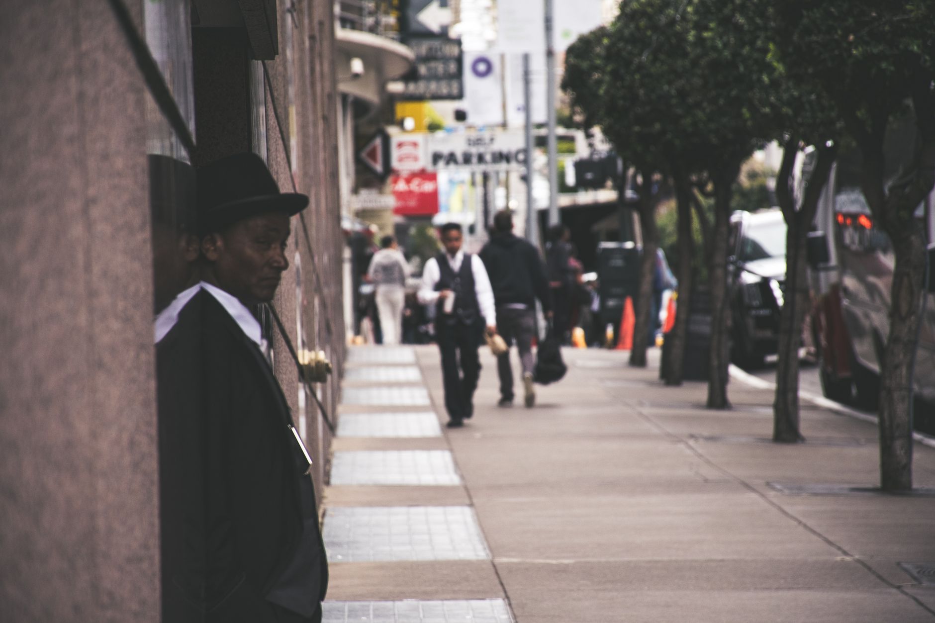 A man in a suit and hat leans against a city building, observing pedestrians. — Pinksale Token: The Latest Innovation in the