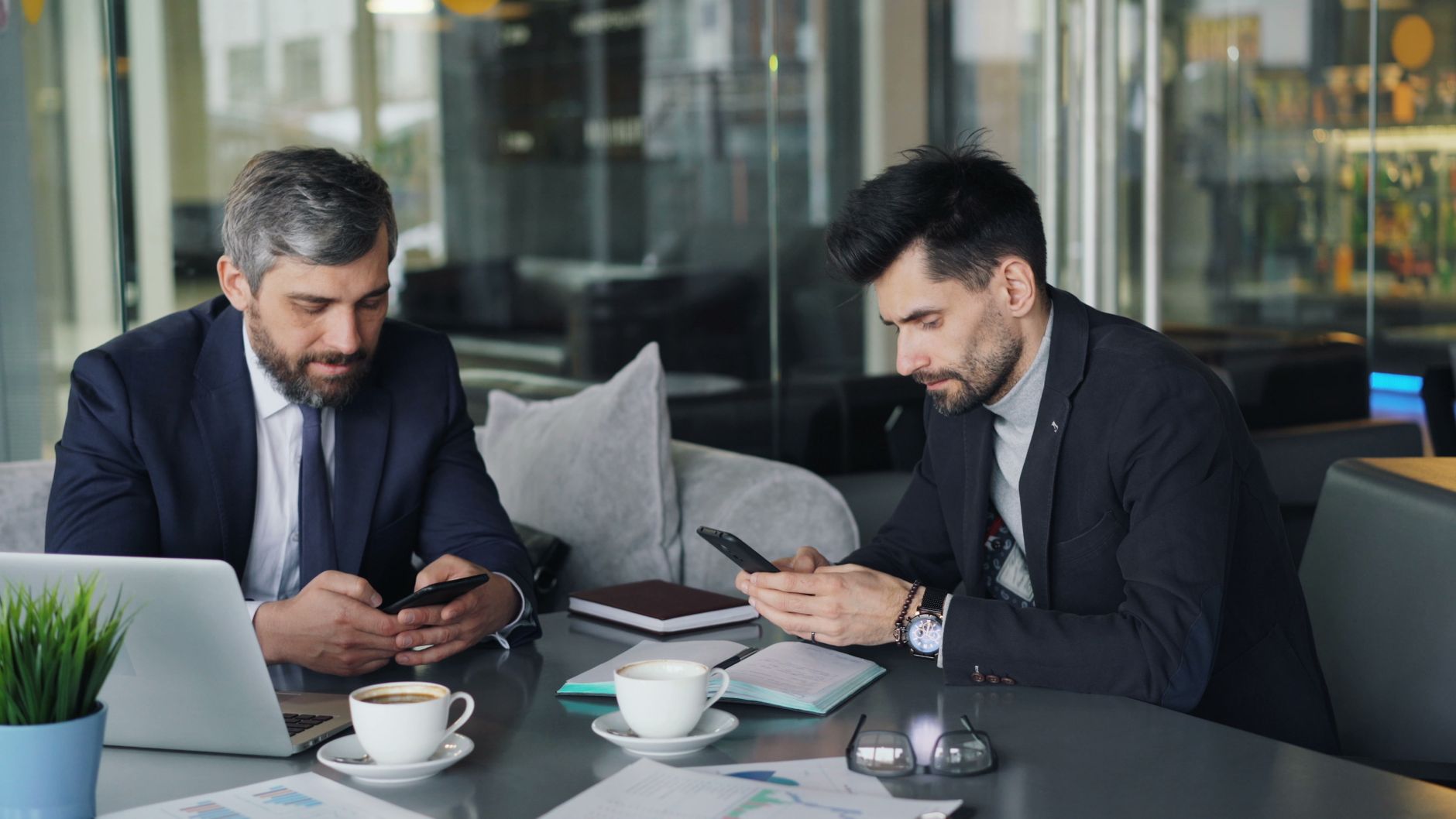 Two businessmen in a cafe working on smartphones and laptops, engaged in a meeting. — Shopping for Tren? The Top Retailers Yo