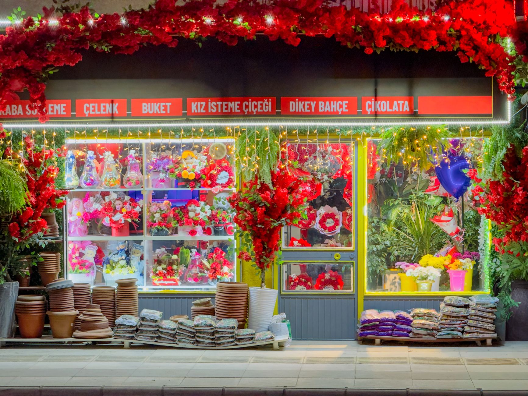 A vibrant floral shopfront in Elâzığ, Türkiye, illuminated at night with colorful flowers and decorative lighting. — Sichere