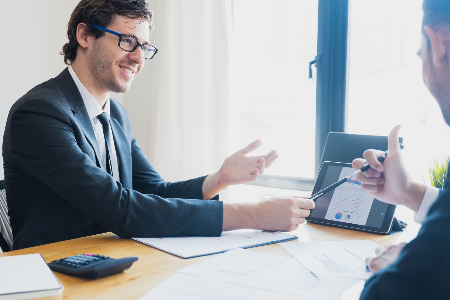 Two businessmen in formal attire discussing a business report in an office setting with a tablet. — A Broker-Dealer F