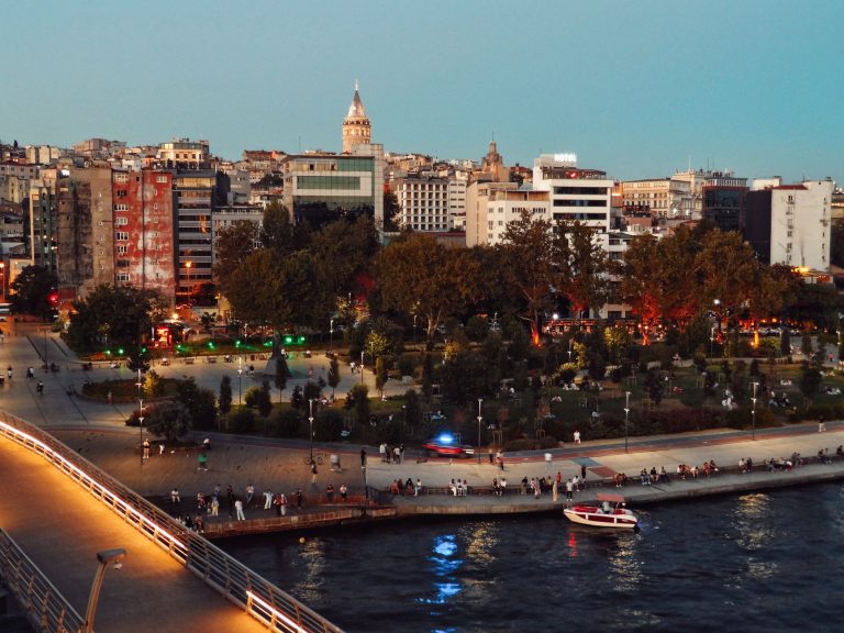 Scenic view of Istanbul's skyline featuring Galata Tower and bustling park at twilight along the waterfront. — Talismania Cas
