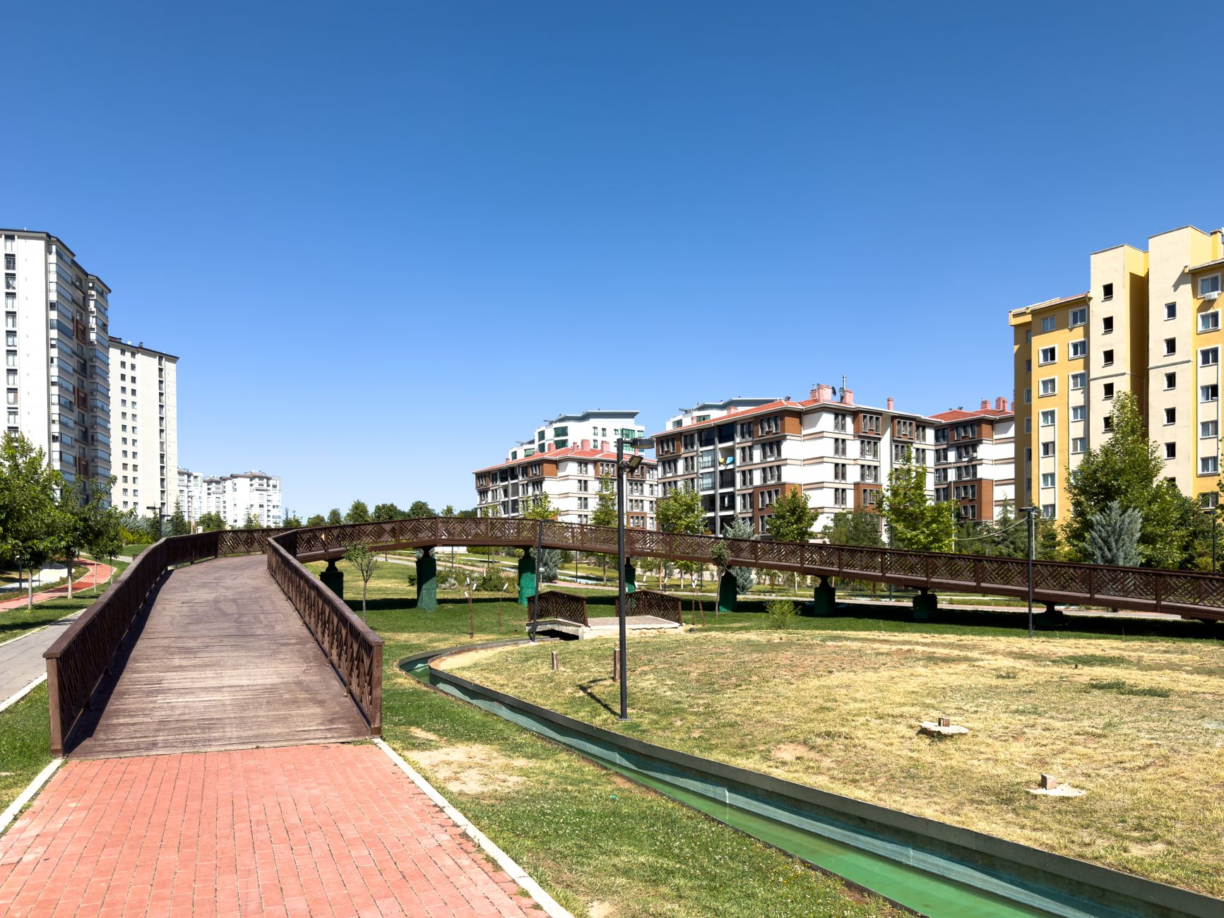 A sunny day in an urban park with modern buildings and a wooden bridge in Elâzığ, Türkiye. — The Best Lightweight samsonite L