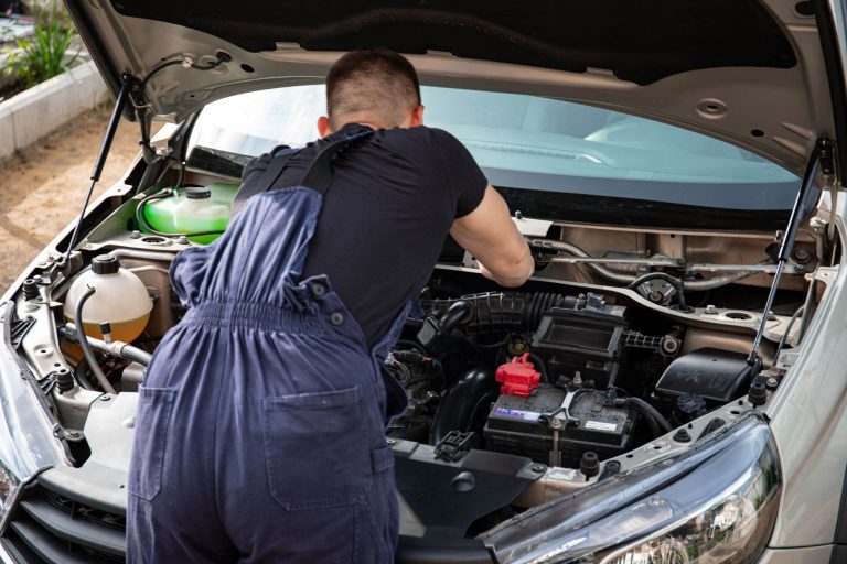 Mechanic in blue coveralls performing car engine maintenance outdoors. — The Innovations Driving Recycle LDPE Processes Forwa