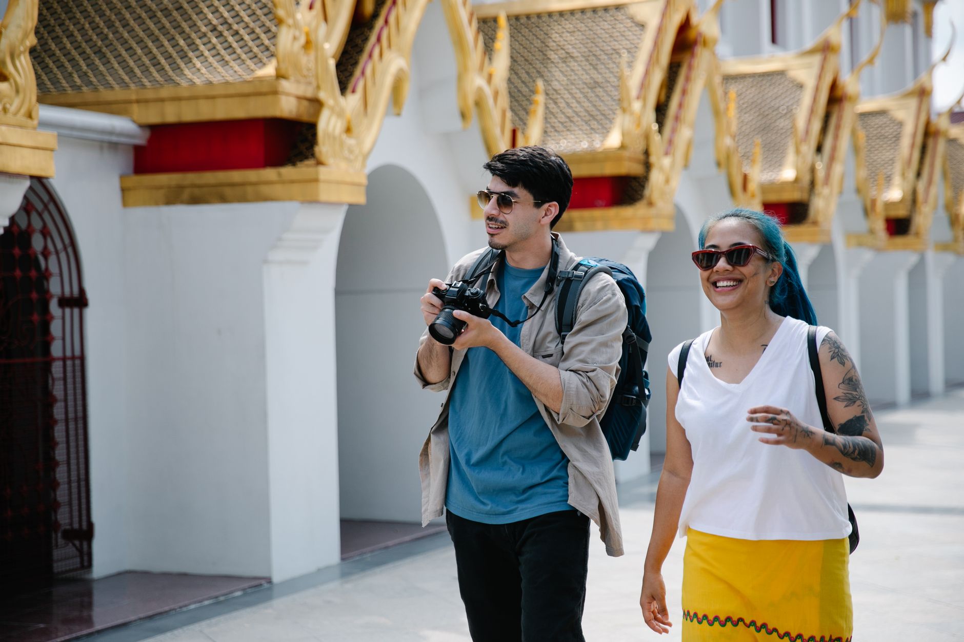 Two tourists with backpacks and cameras enjoy a sunny day exploring ornate Thai architecture. — What Is The Best Camera Bags