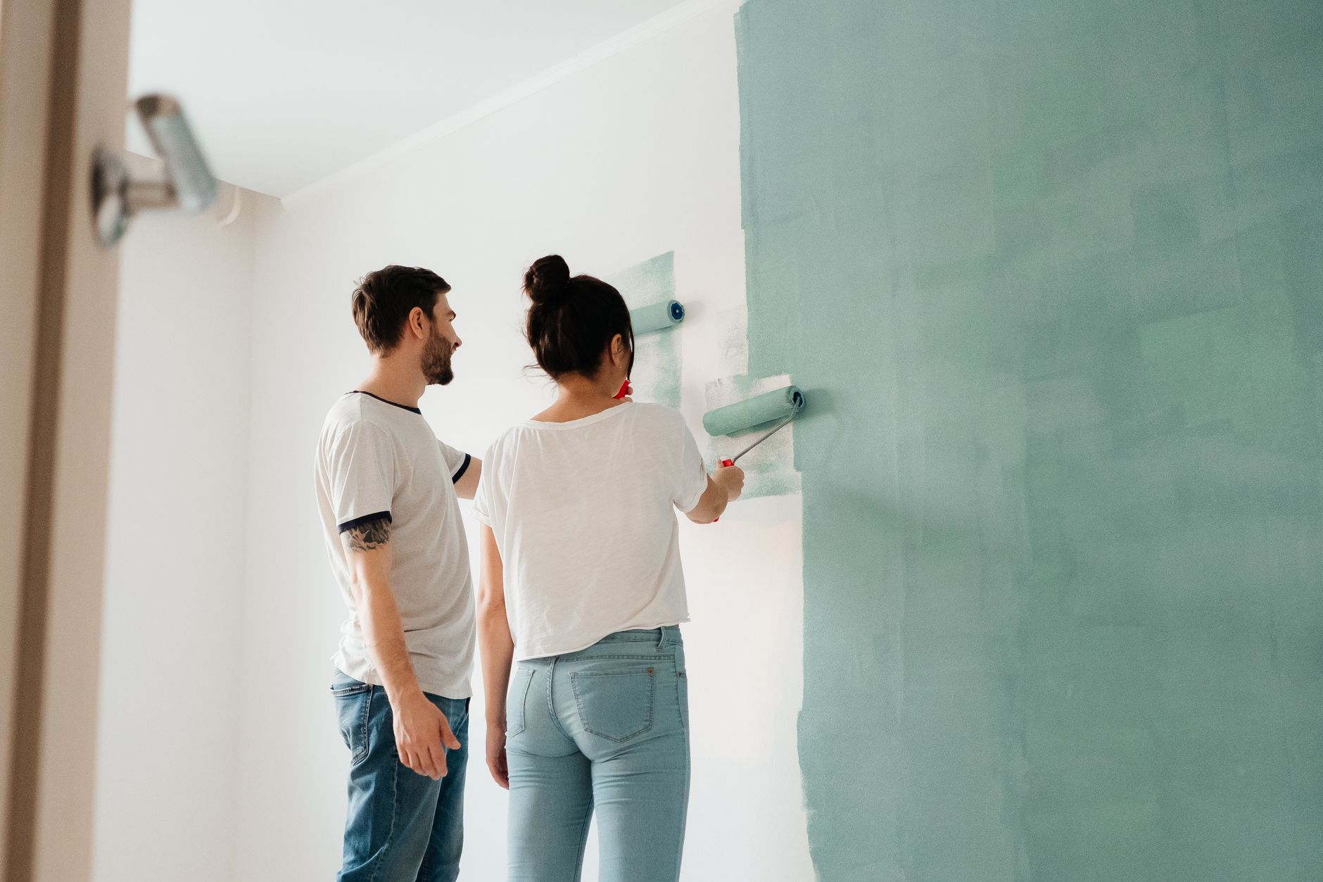 A couple collaborates to paint a wall with a roller indoors, showcasing teamwork. — When Do You Hire an Emergency Plumber?