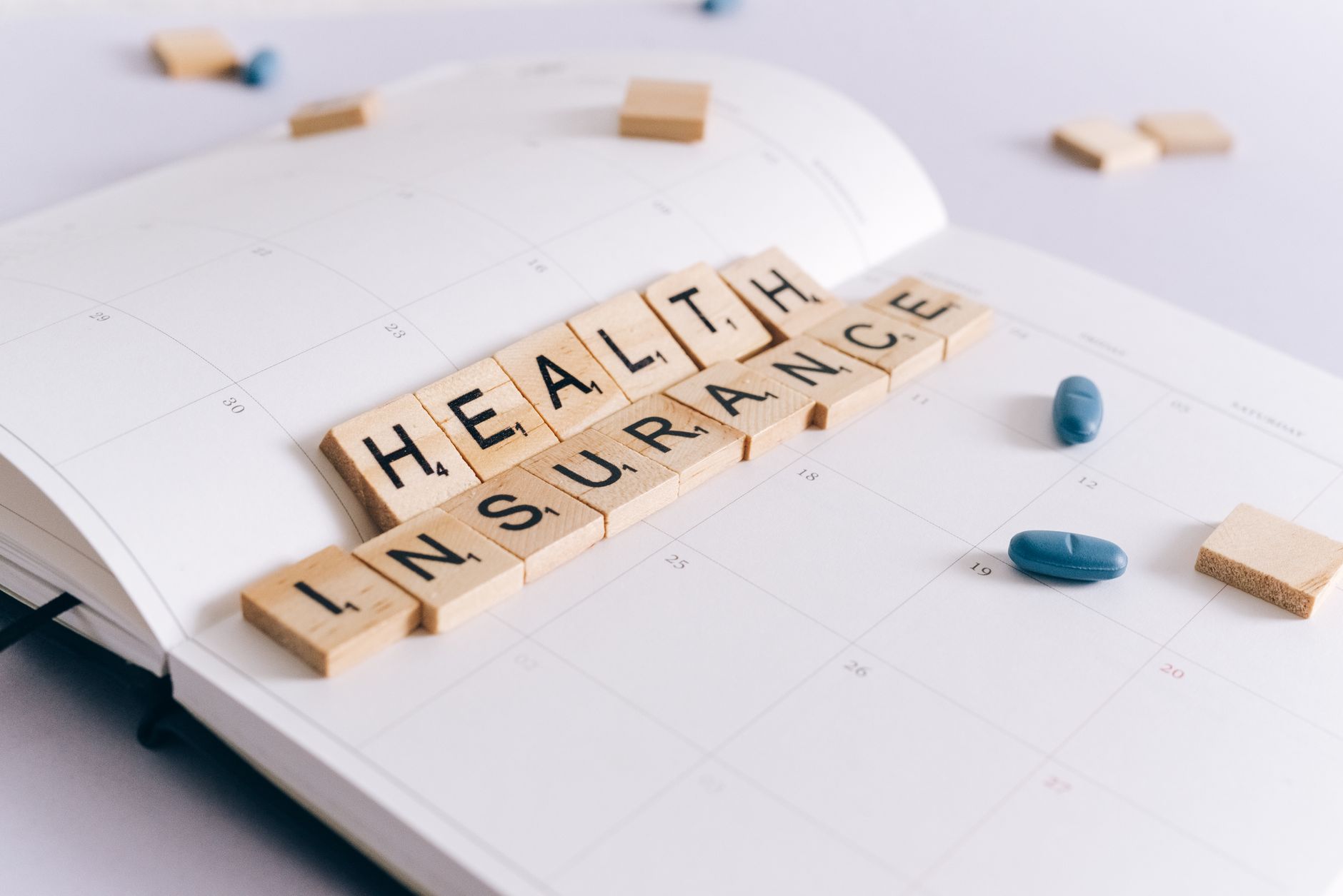 Scrabble tiles spelling 'Health Insurance' on a calendar with pills. — Whether The Dope Abuse Leave The Individual To Maintai