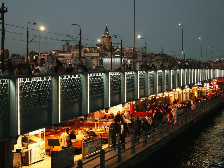 Night view of Galata Bridge bustling with people and distant Galata Tower in Istanbul. — Wie hoch ist der Willkommensbonus be