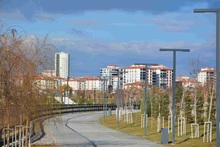 An empty urban park pathway lined with trees, lampposts, and modern residential buildings. — Wie hoch sind die Einzahlungsopt